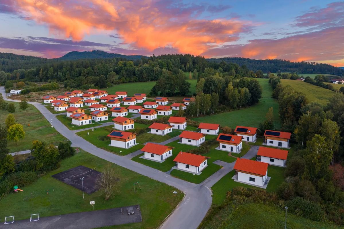 Luftbild: Ferienhäuser mit roten Dächern vor Wald und Bergen