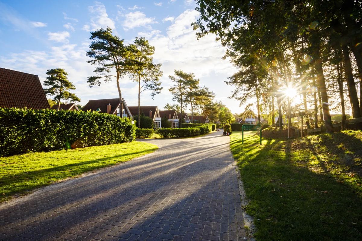 Weg zwischen Bäumen und Ferienhäusern im Abendlicht