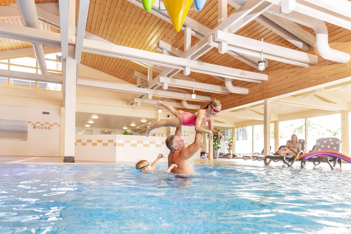 Familie im Hallenbad unter einem Holzdach
