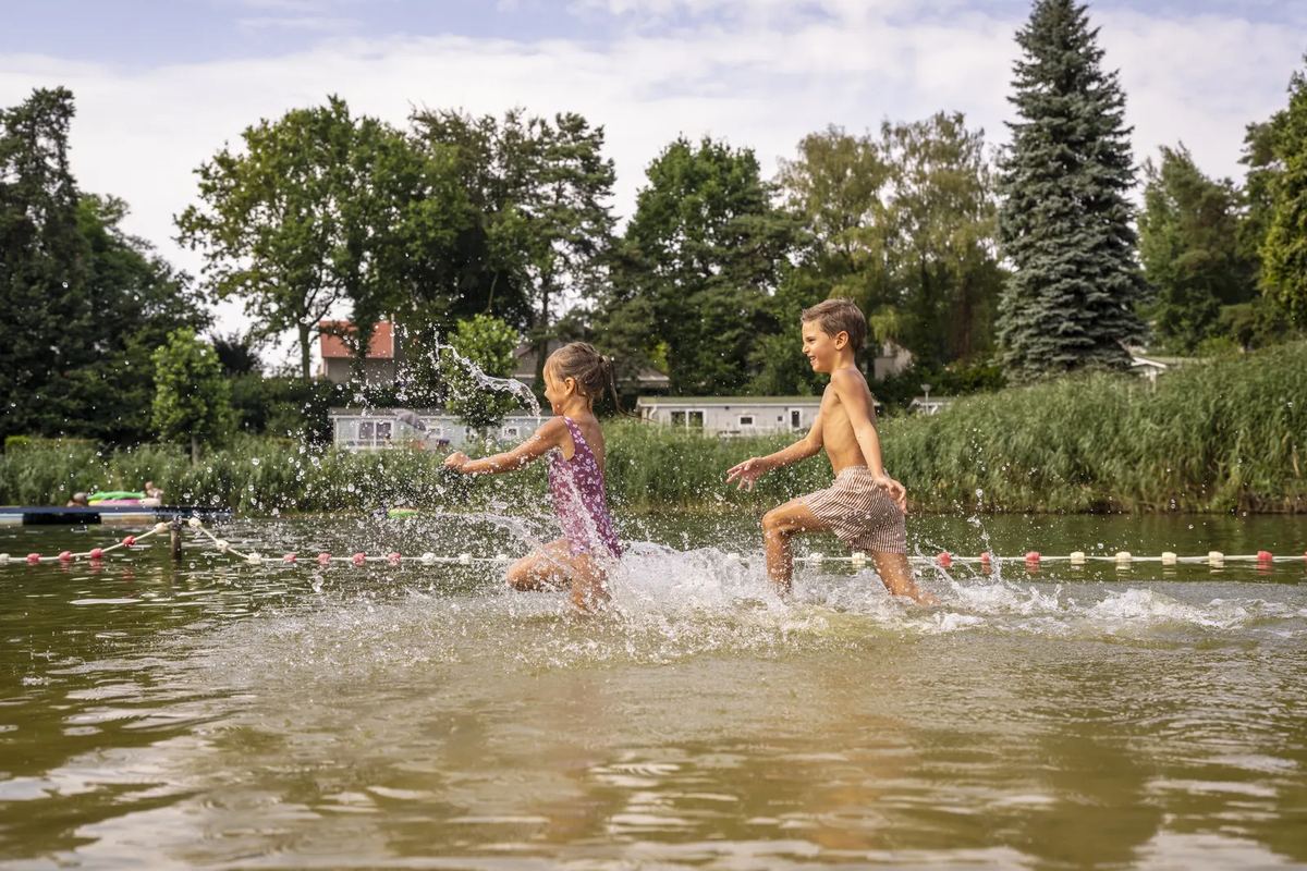 Kinder rennen durchs flache Wasser des Badesees