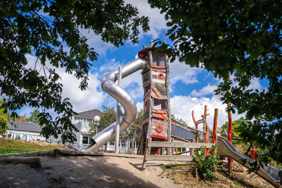 Spielturm mit langer Rutsche zwischen Bäumen